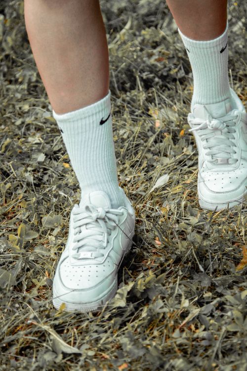Free Close-up of a person's legs wearing white sneakers and socks on a grassy path. Stock Photo