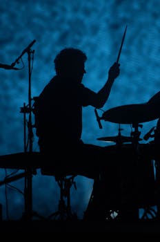 Silhouette of a drummer performing on stage with a blue lit background. Dynamic live music scene.