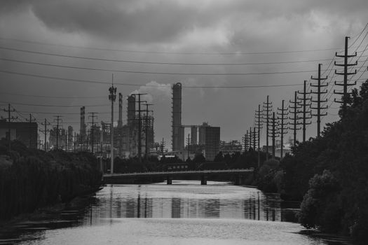 Moody black and white photo of an industrial river scene with power lines and factories.