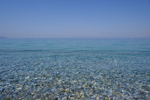 Free Tranquil pebble beach with clear blue waters under a bright summer sky. Stock Photo