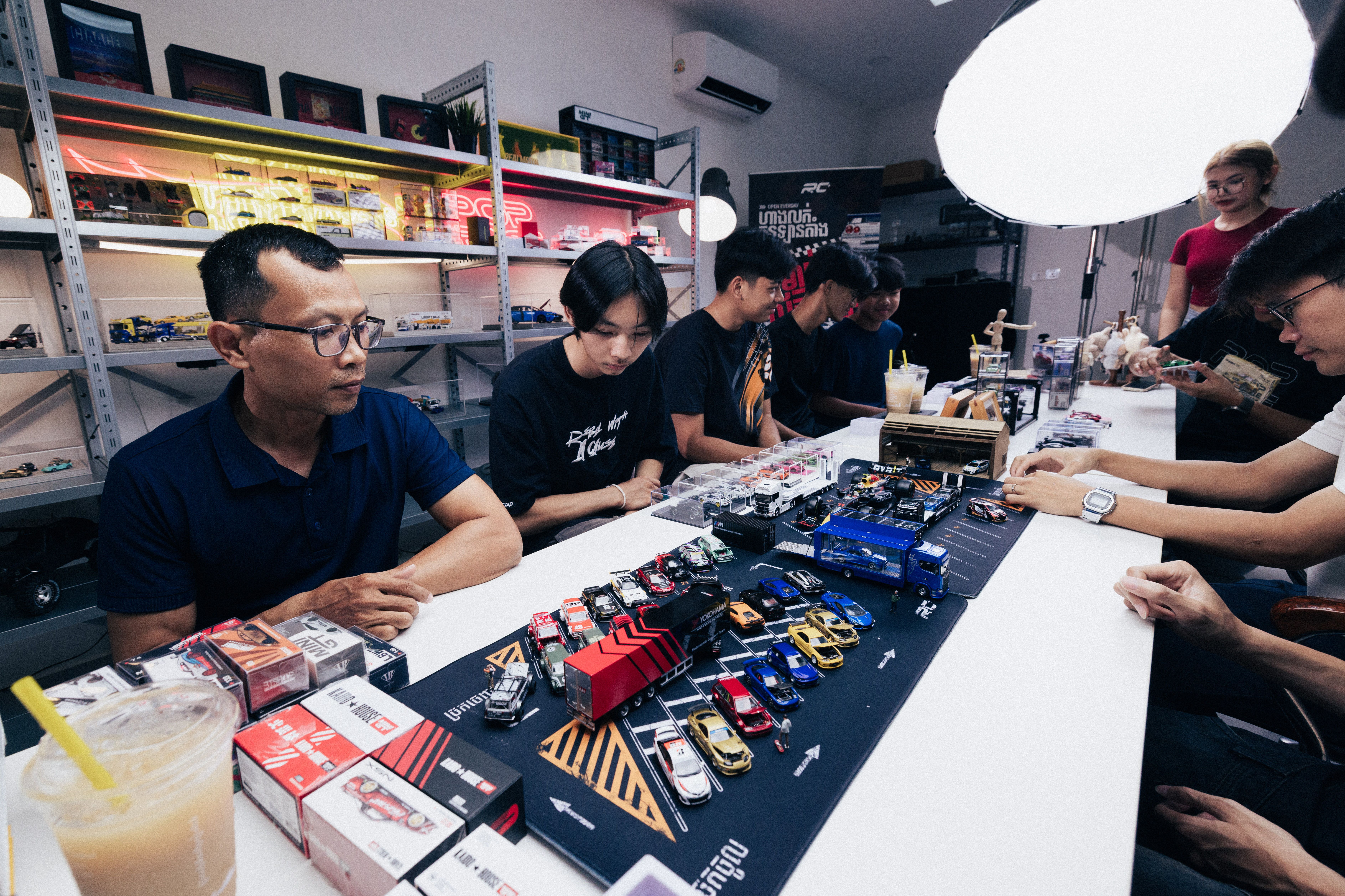 A group of hobbyists enjoying scale model cars in a well-lit store with shelves of miniatures.