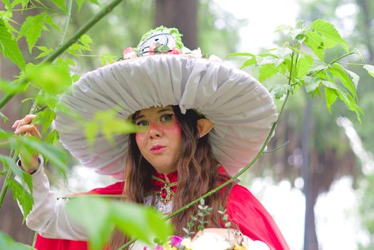 A person in a whimsical fantasy costume stands among lush greenery, embodying a magical character.
