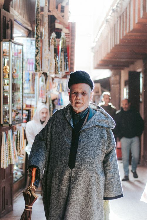 Free An elderly man in traditional attire strolls through a vibrant Moroccan market street, capturing cultural essence. Stock Photo