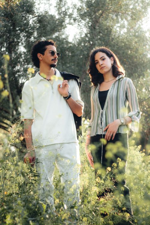Free A fashionable young couple standing in a sunlit field surrounded by greenery. Stock Photo