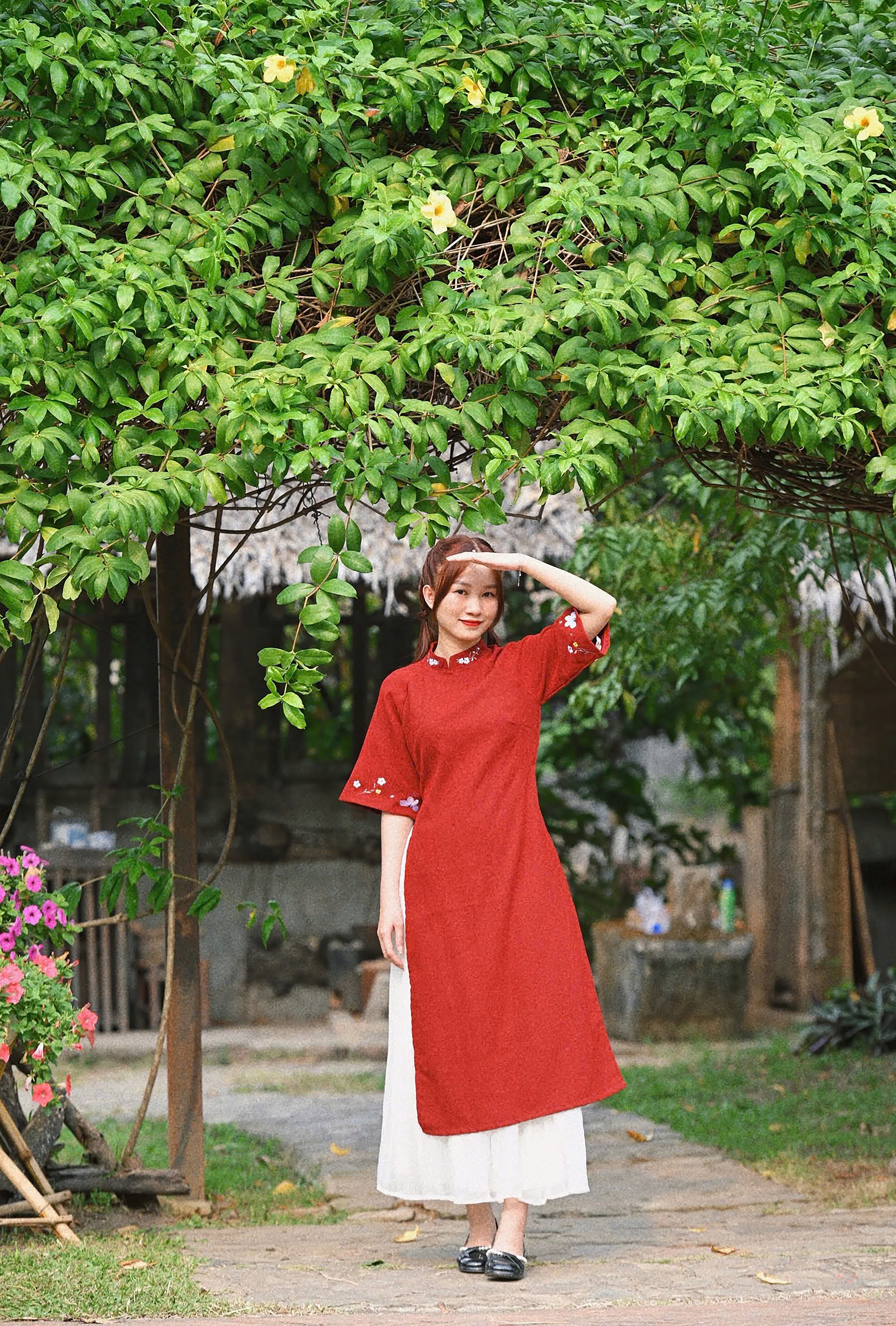 A young woman wearing a red áo dài in a lush garden setting in Ho Chi Minh City.