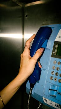 Detailed shot of a hand lifting a blue payphone receiver inside a booth, evoking nostalgia.