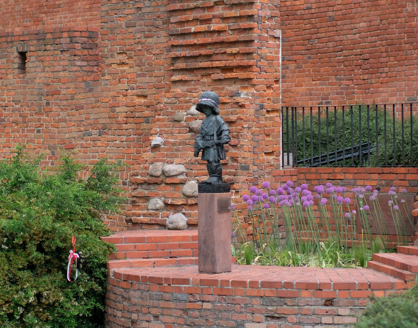 Statue of Little Insurgent among flowers and brick walls in Warsaw, Poland.