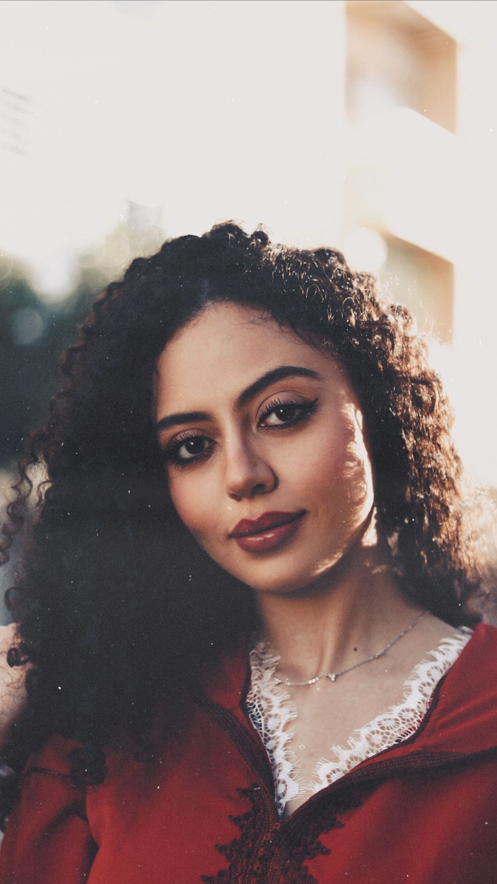 Elegant portrait of a woman with curly hair, wearing a red outfit, captured in warm sunset light.