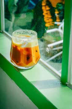 Refreshing iced latte placed on a bright window sill with sunlight streaming in, casting inviting shadows.