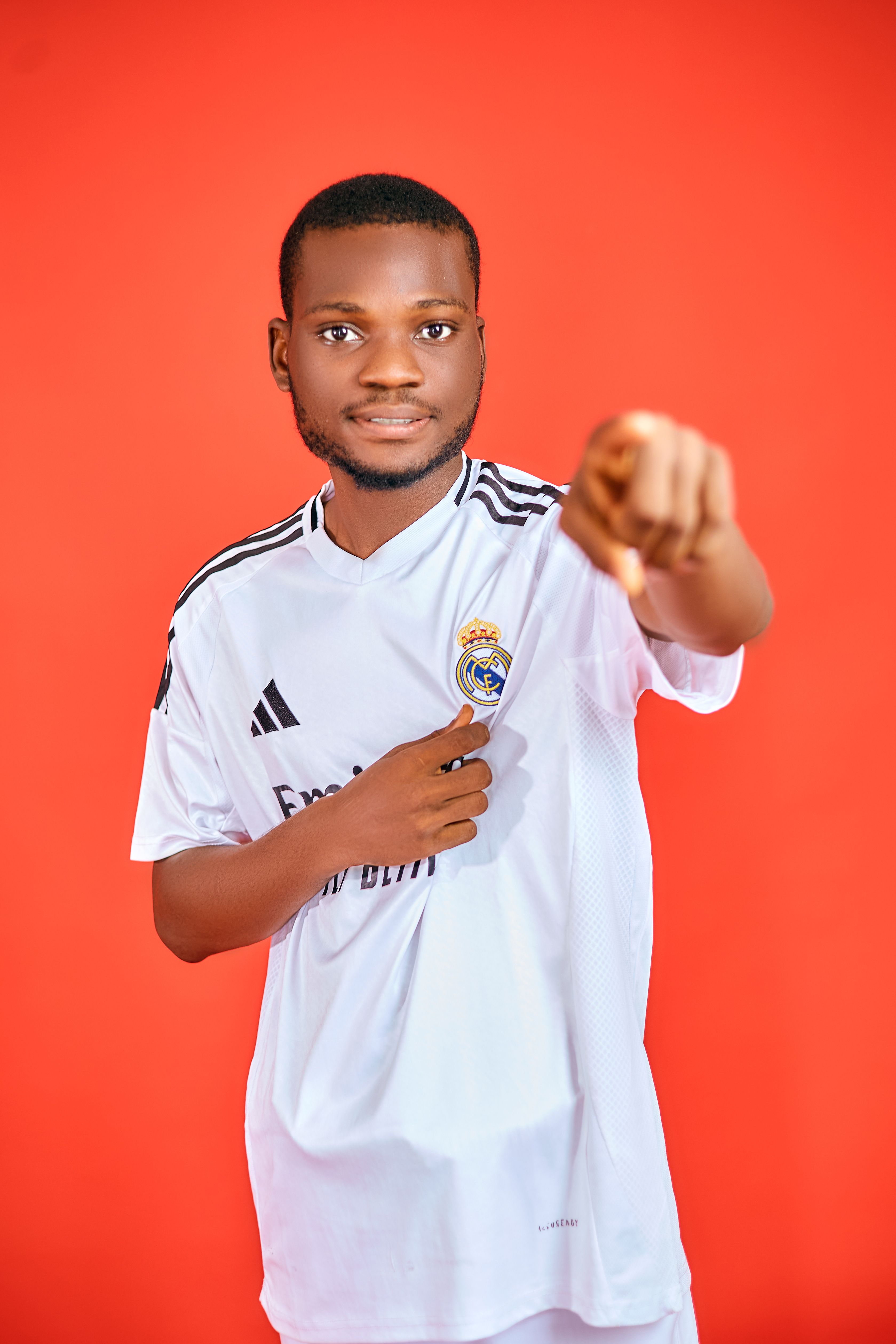 Confident young man in a sports jersey on a red background pointing at the camera