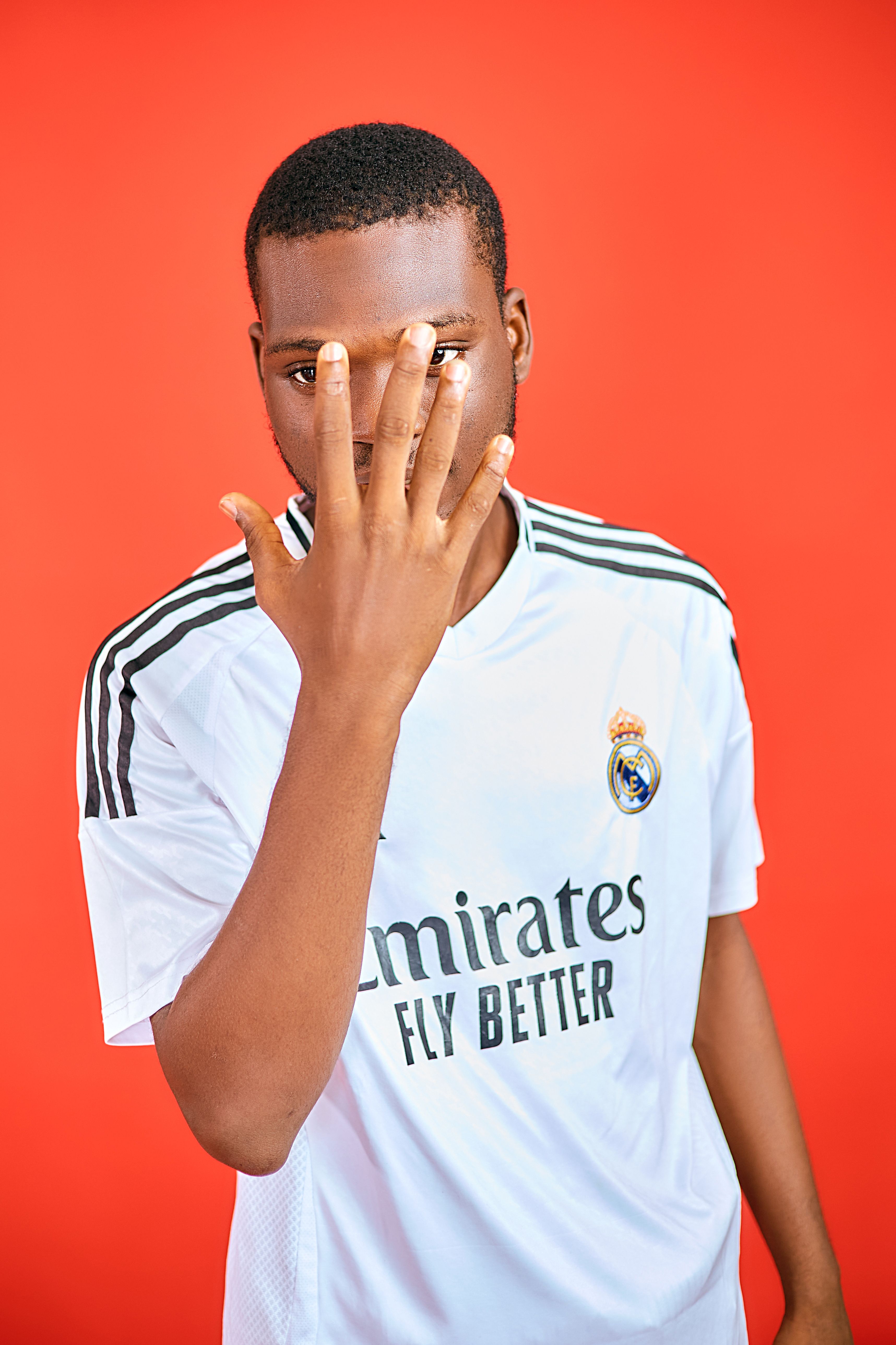 Portrait of a young man in a sports jersey posing against a red background with a unique hand gesture.