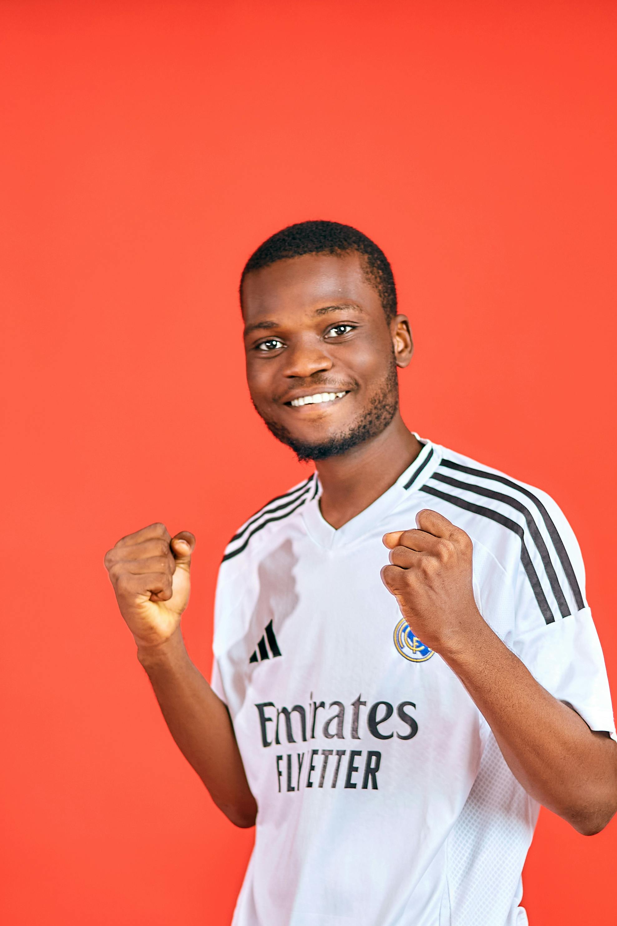 Portrait of a joyful young man celebrating in a soccer jersey against a red background.