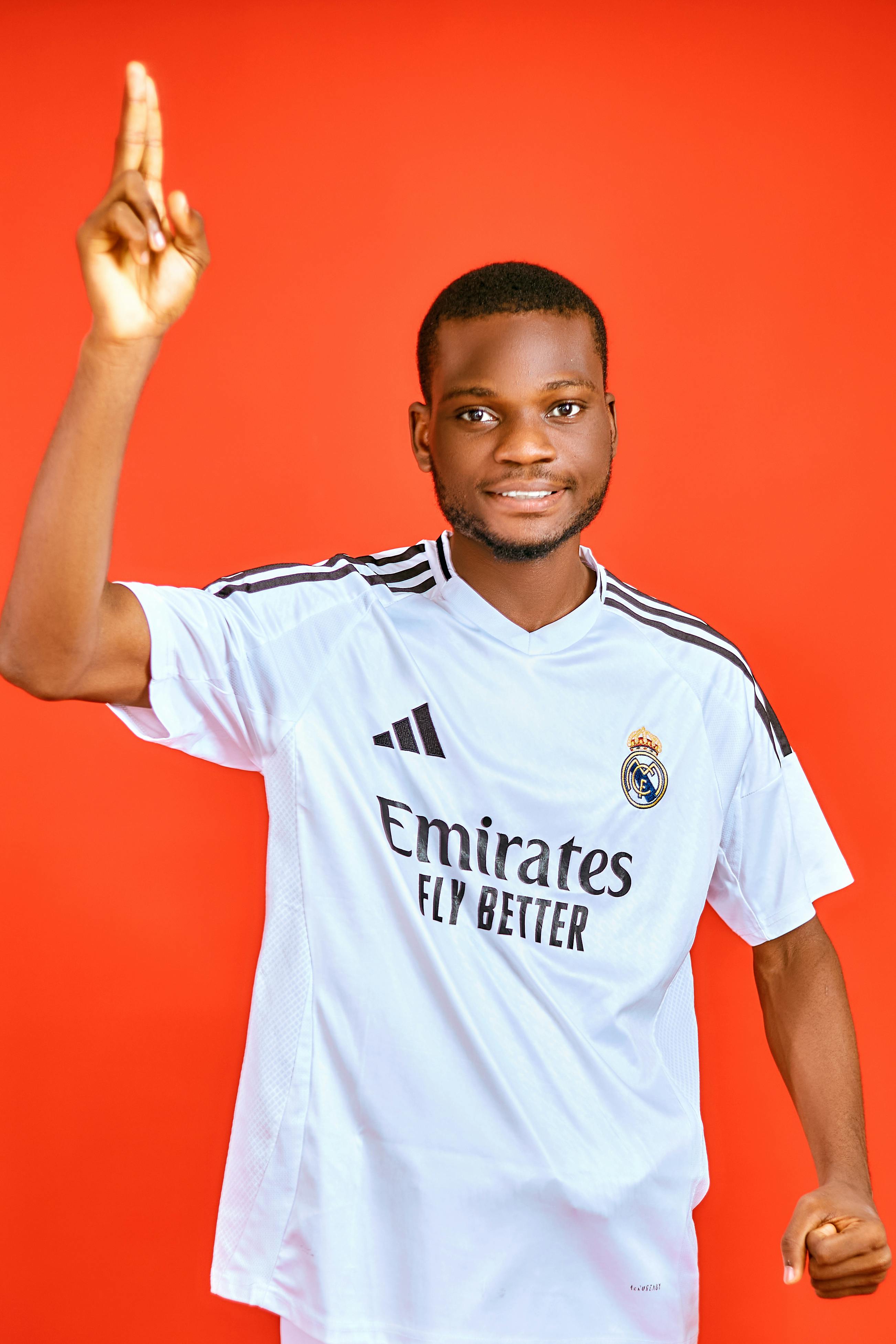 Confident young man wearing a soccer jersey with an enthusiastic gesture against a red backdrop.