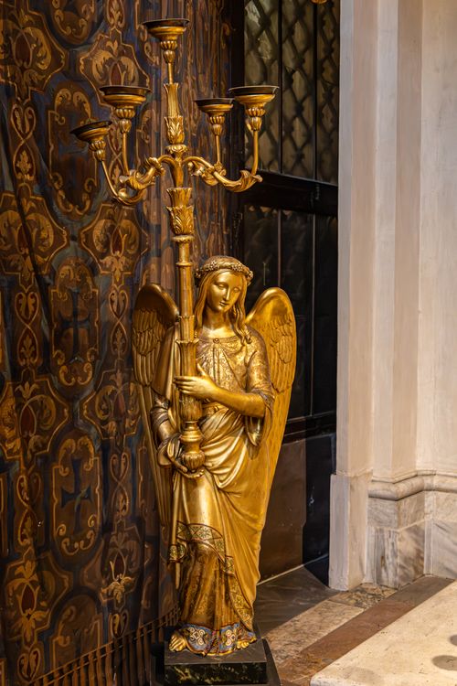 Free Intricate golden angel statue elegantly holding a candelabra inside an ornate Italian church setting. Stock Photo