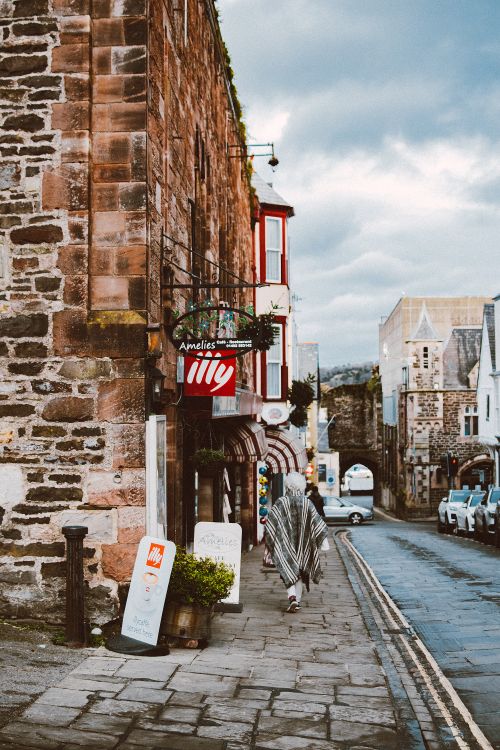 Free A scenic view of a cobblestone street in a historic town with shops and a passerby. Stock Photo
