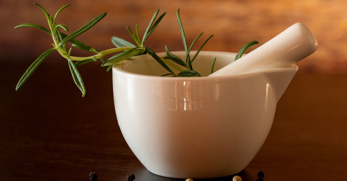 A stone mortar and pestle with fresh herbs on a wooden surface