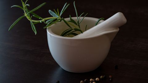 Elegant white porcelain mortar with fresh rosemary and peppercorns on a wooden surface.