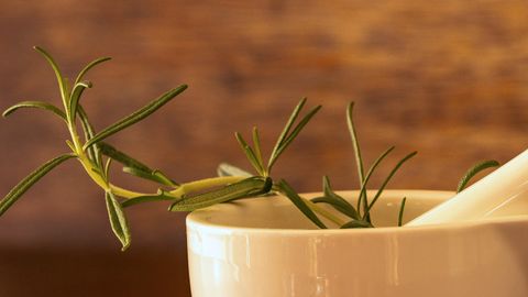 White porcelain mortar with rosemary sprig and peppercorns on wooden surface.
