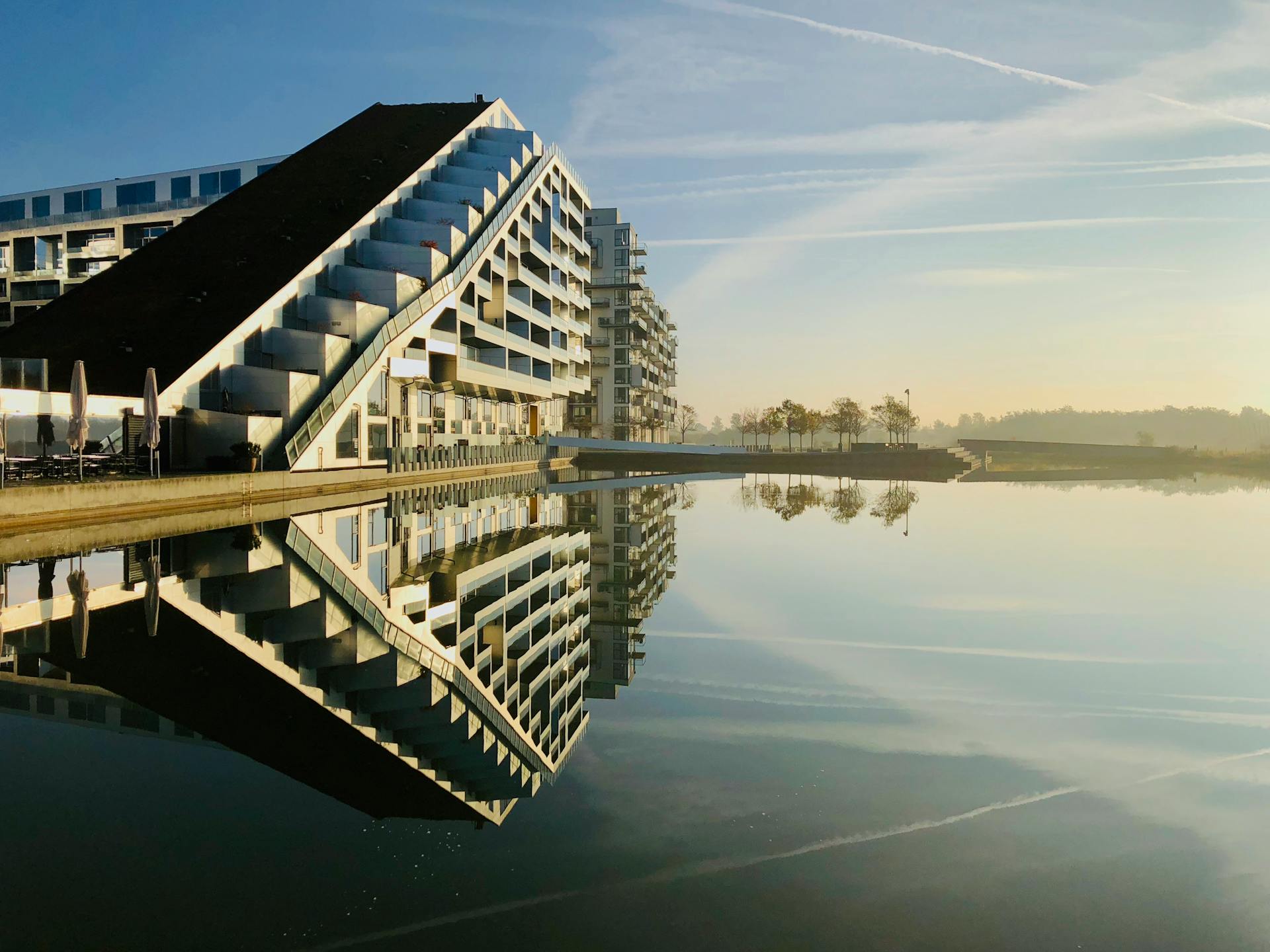 A futuristic building in Copenhagen reflecting on calm waters at dawn, showcasing modern architecture.