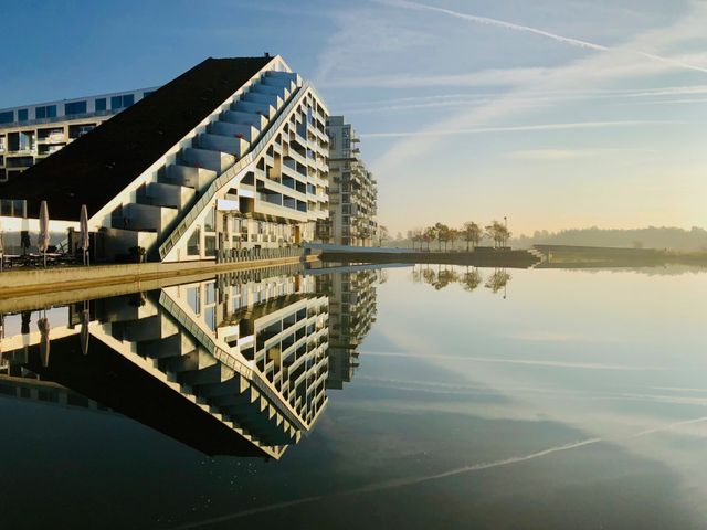 A futuristic building in Copenhagen reflecting on calm waters at dawn, showcasing modern architecture.