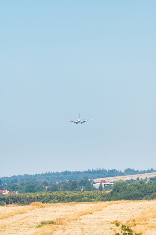 Free An airplane approaches Poprad, Slovakia, flying over golden fields under a clear blue sky. Stock Photo