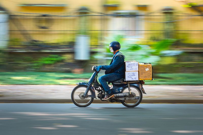 Side view of a motorcycle courier speeding down a road with packages in motion blur background.