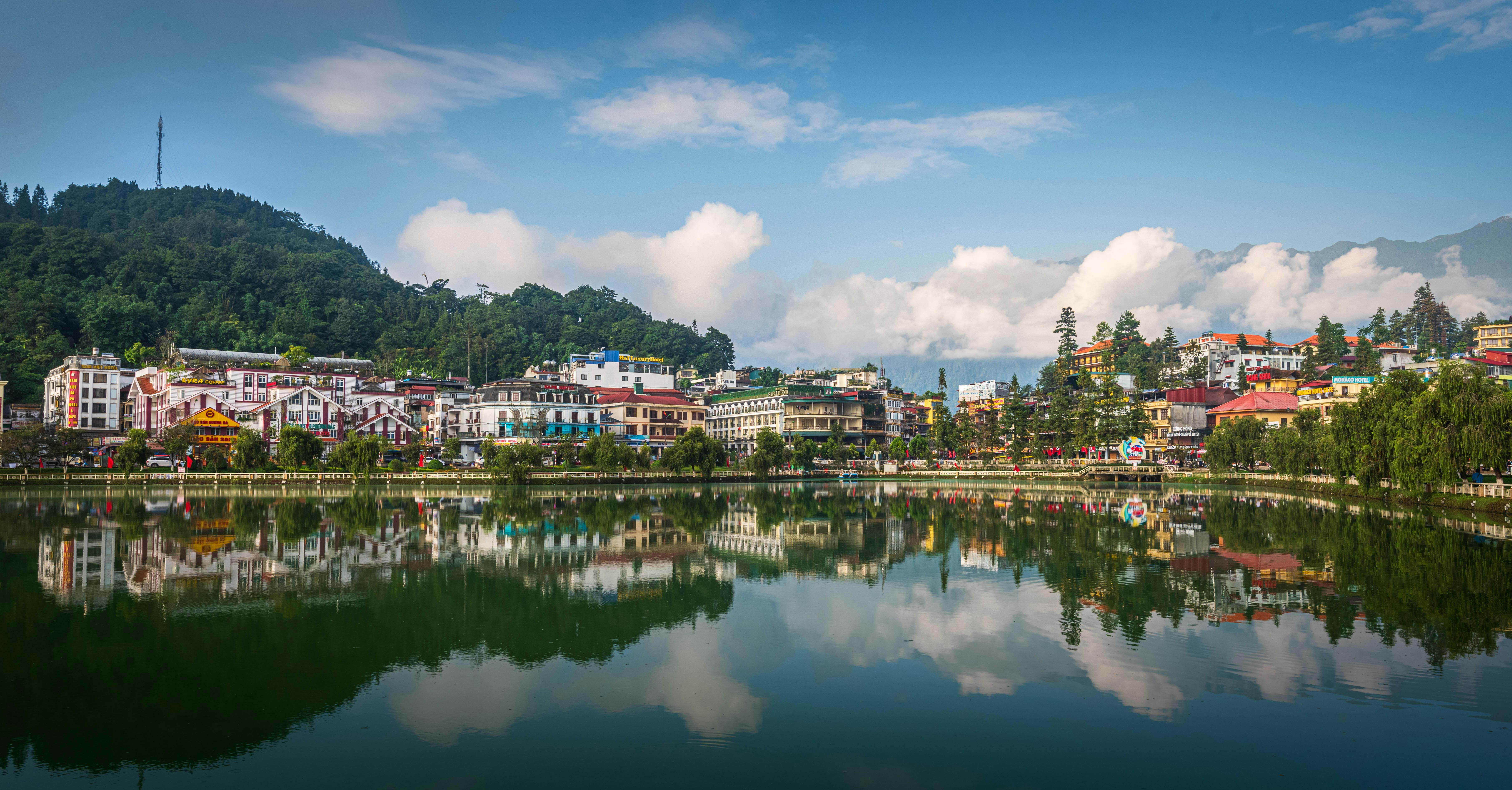 Stunning view of Sapa town reflecting in a serene lake surrounded by lush greenery and blue skies.