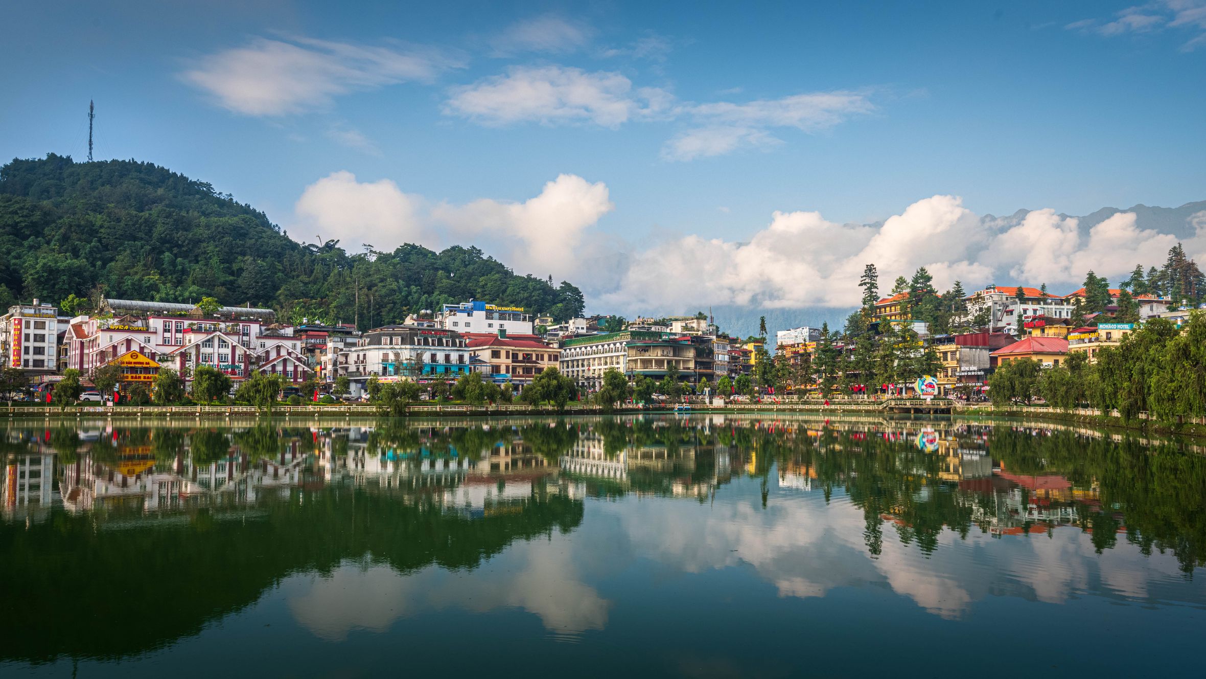 Stunning view of Sapa town reflecting in a serene lake surrounded by lush greenery and blue skies.