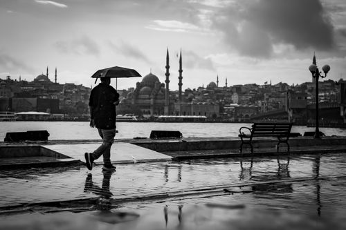 Free A person walks with an umbrella along İstanbul's waterfront, featuring a classic skyline view. Stock Photo