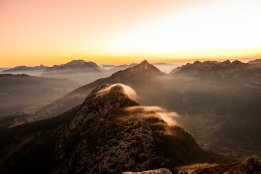 Stunning sunset view of majestic mountains with mist and golden light. Ideal for travel and adventure themes.