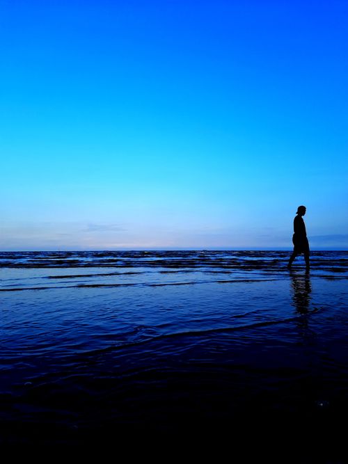 Free Peaceful silhouette of person walking beside ocean during twilight. Stock Photo