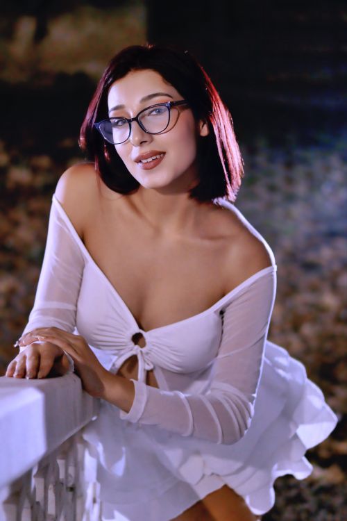 Free Elegant woman in white dress with glasses posing confidently at night outdoors. Stock Photo