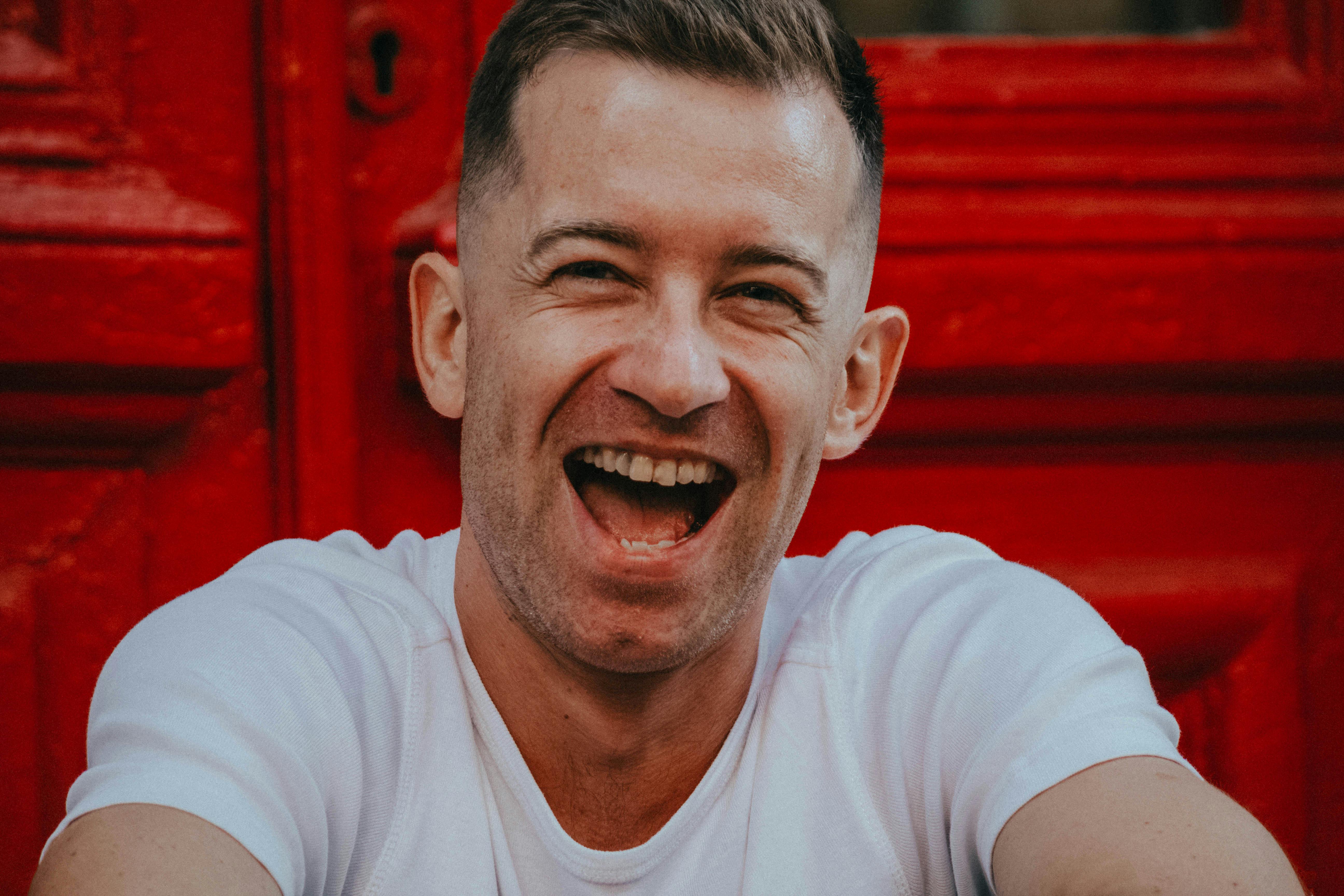 De franc Retrat d'un home alegre que riu davant d'una porta vermella vibrant. Foto d'estoc