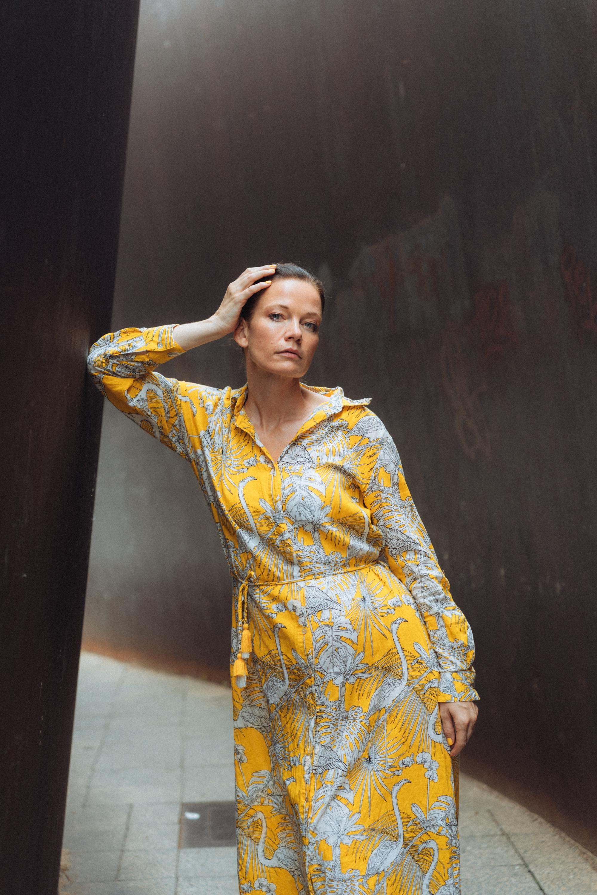 Free Woman in a floral yellow dress leaning against a wall in an outdoor setting. Stock Photo