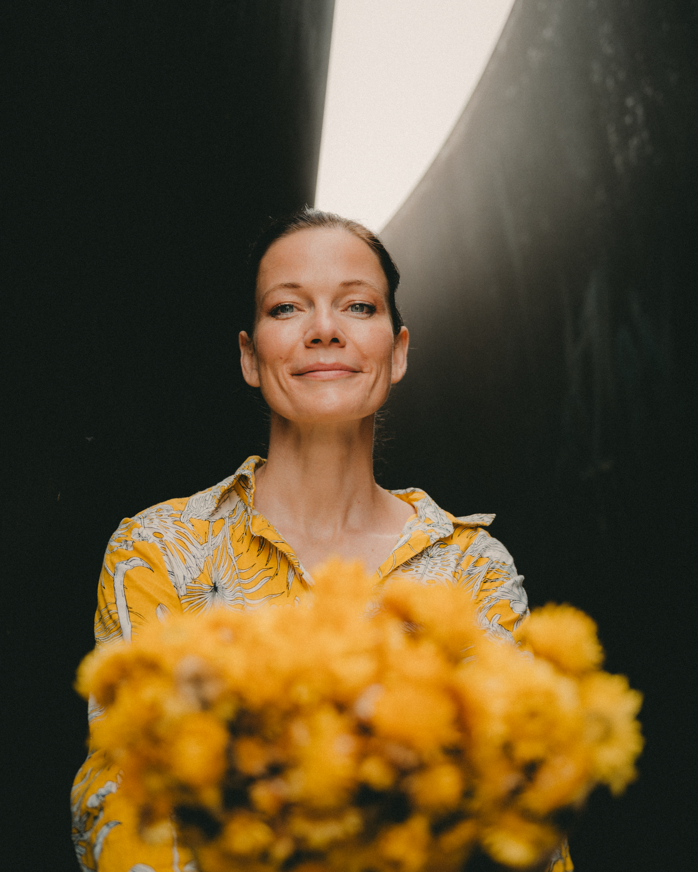 Portrait of a smiling woman holding a bouquet of yellow flowers in soft lighting.