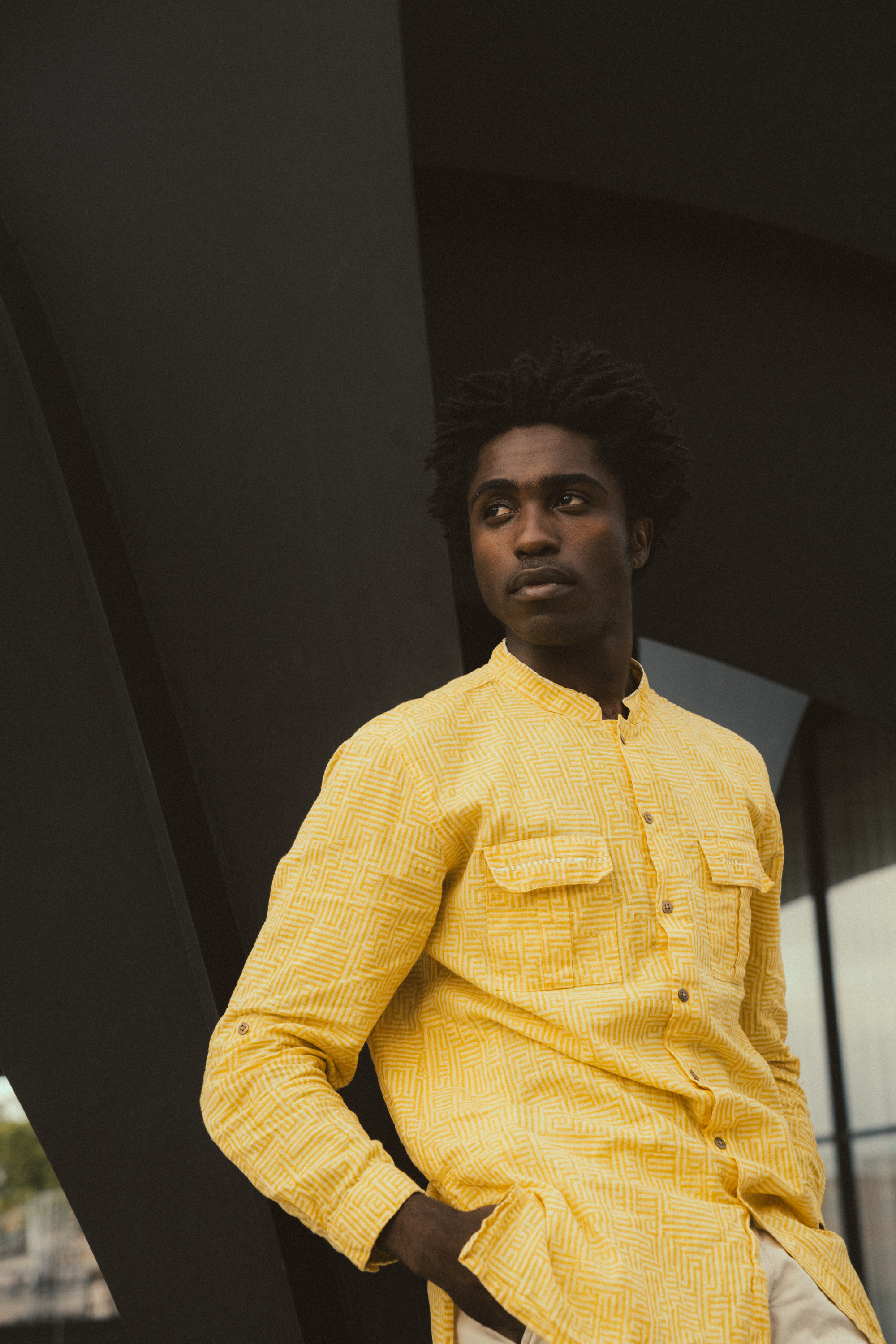 Portrait of a stylish young man wearing a yellow shirt, captured outdoors with a modern architectural background.