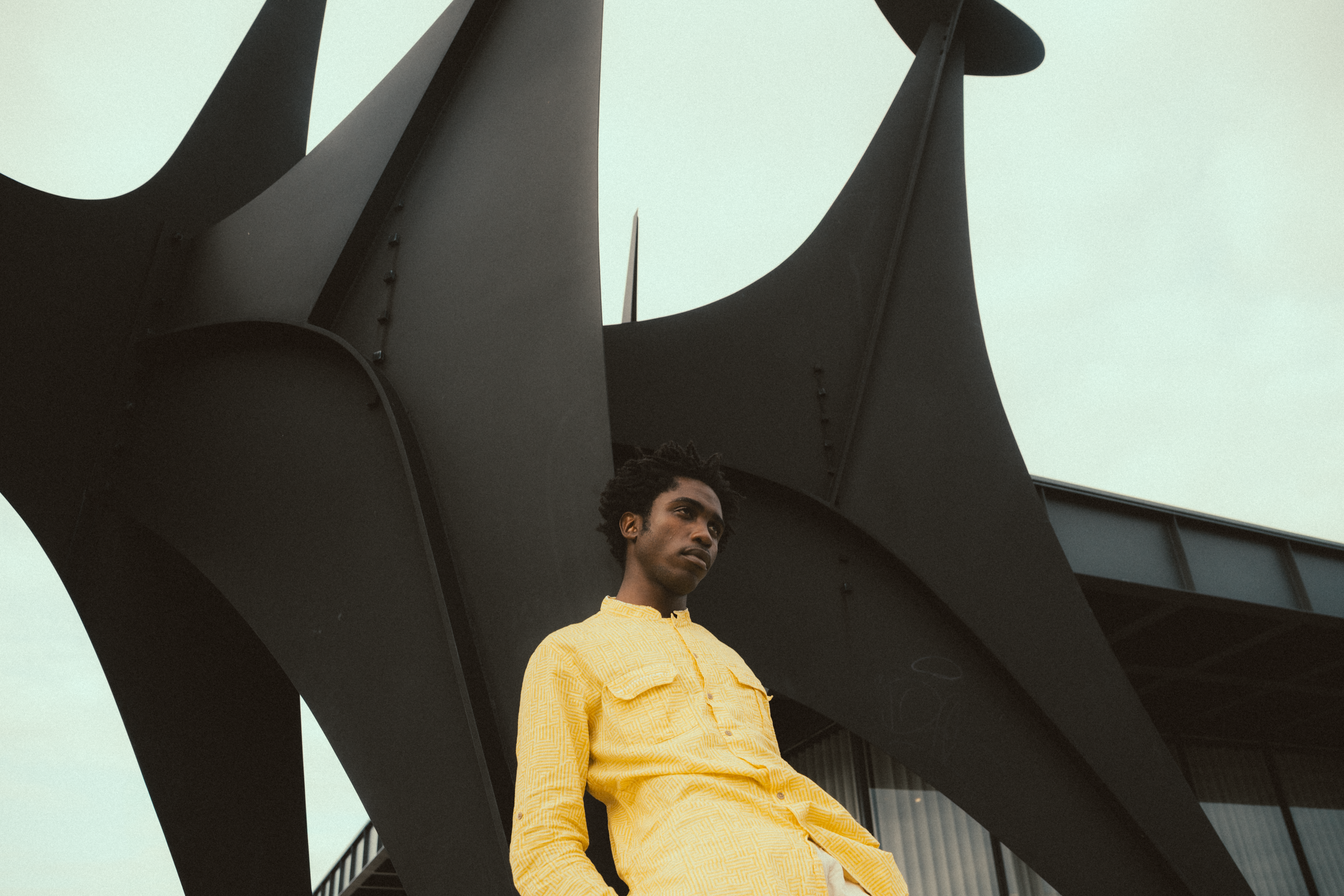 Portrait of a person in a yellow shirt standing against modern sculpture.