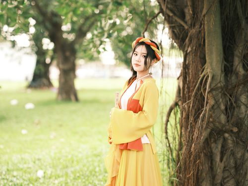 Free A portrait of a young woman in traditional attire standing by a large tree in a lush, green outdoor setting. Stock Photo