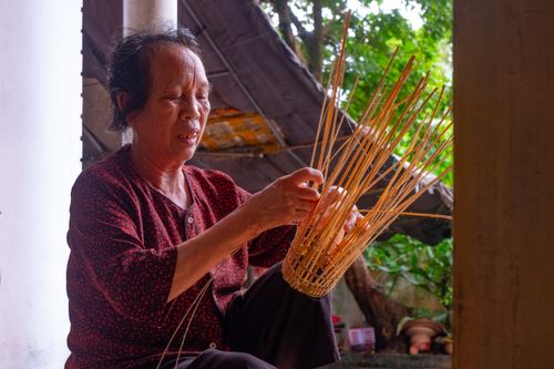 Free An elderly woman skillfully weaves a basket outside her home in Hưng Yên, Vietnam. Stock Photo