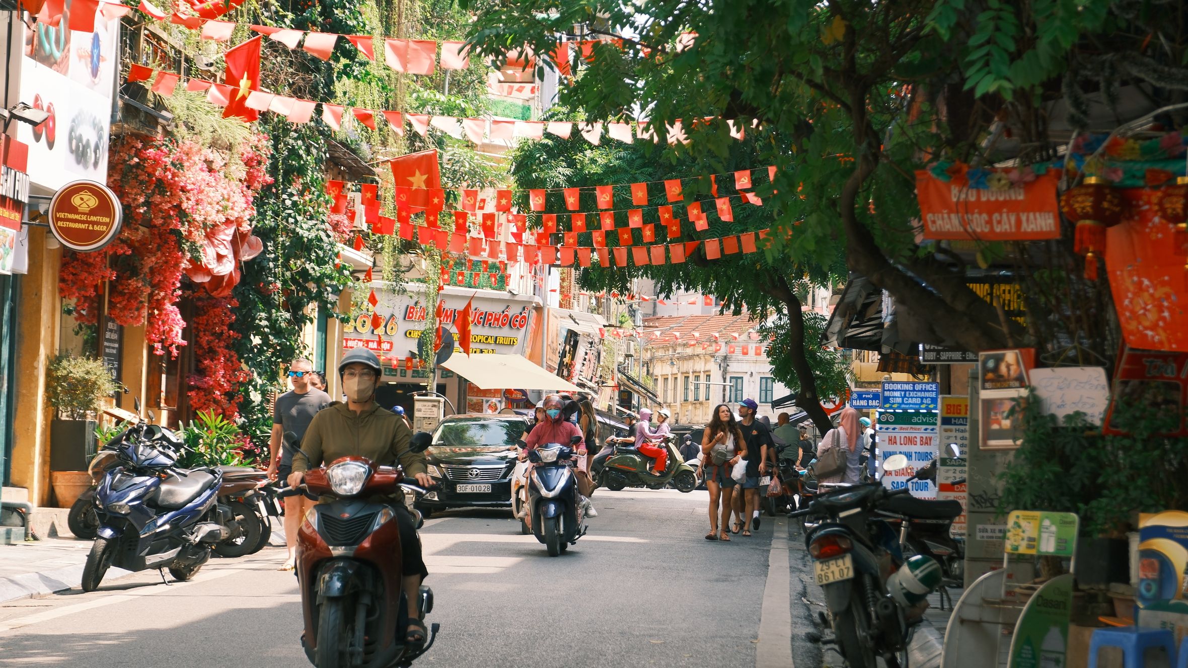 Street scene in Hà Nội featuring locals on motorcycles and colorful decorations.