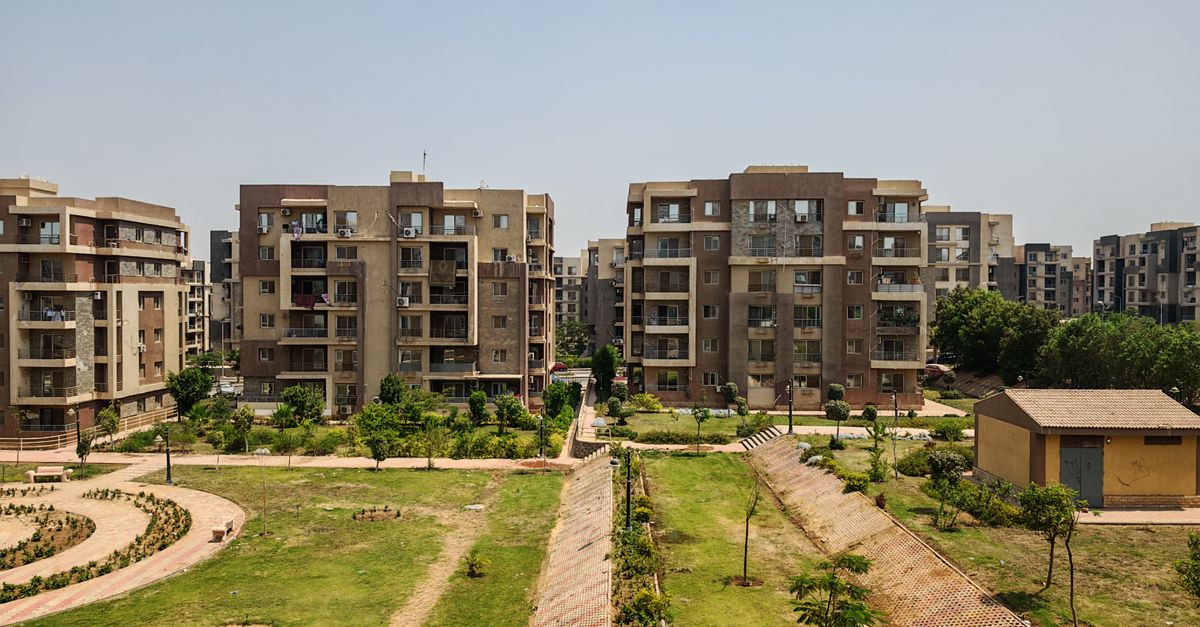 Aerial view of a modern residential complex surrounded by green gardens under a clear sky.