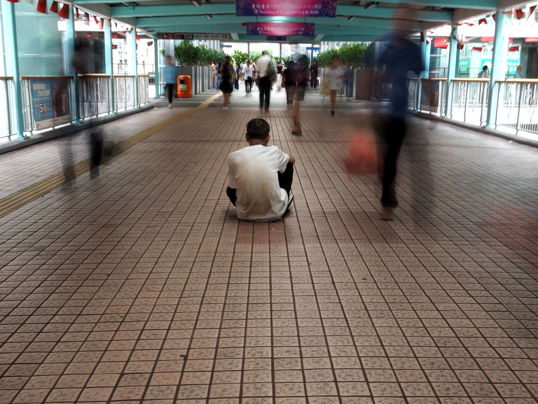 手機街拍禮儀全指南:隱私保護、拍攝許可與發布規範 A solitary figure seated amidst blurred bustling pedestrians in a Hong Kong walkway.