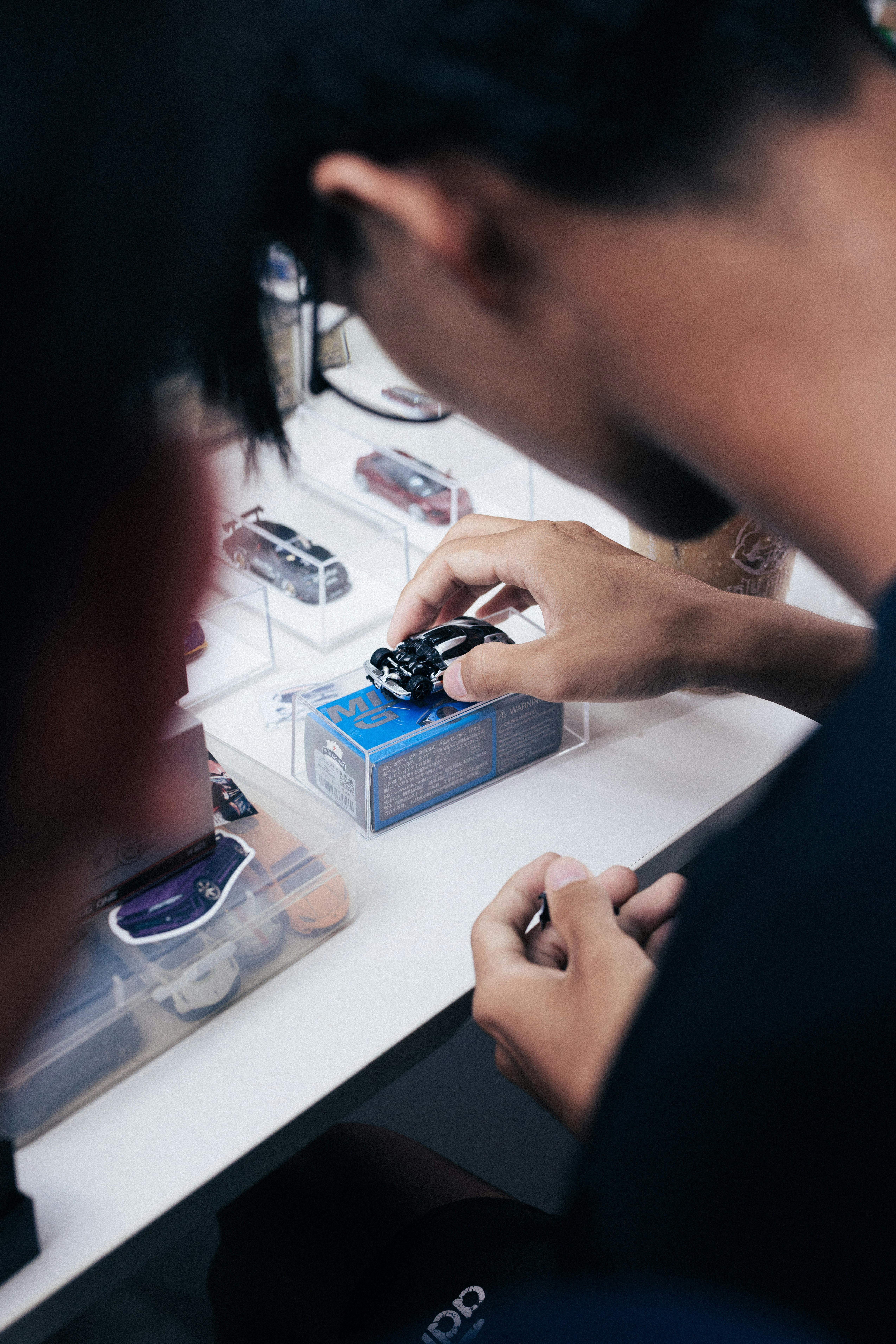 common:alt.prefix Mãos interagindo com modelos de carros em escala durante um encontro em Phnom Penh, Camboja. common:alt.postfix