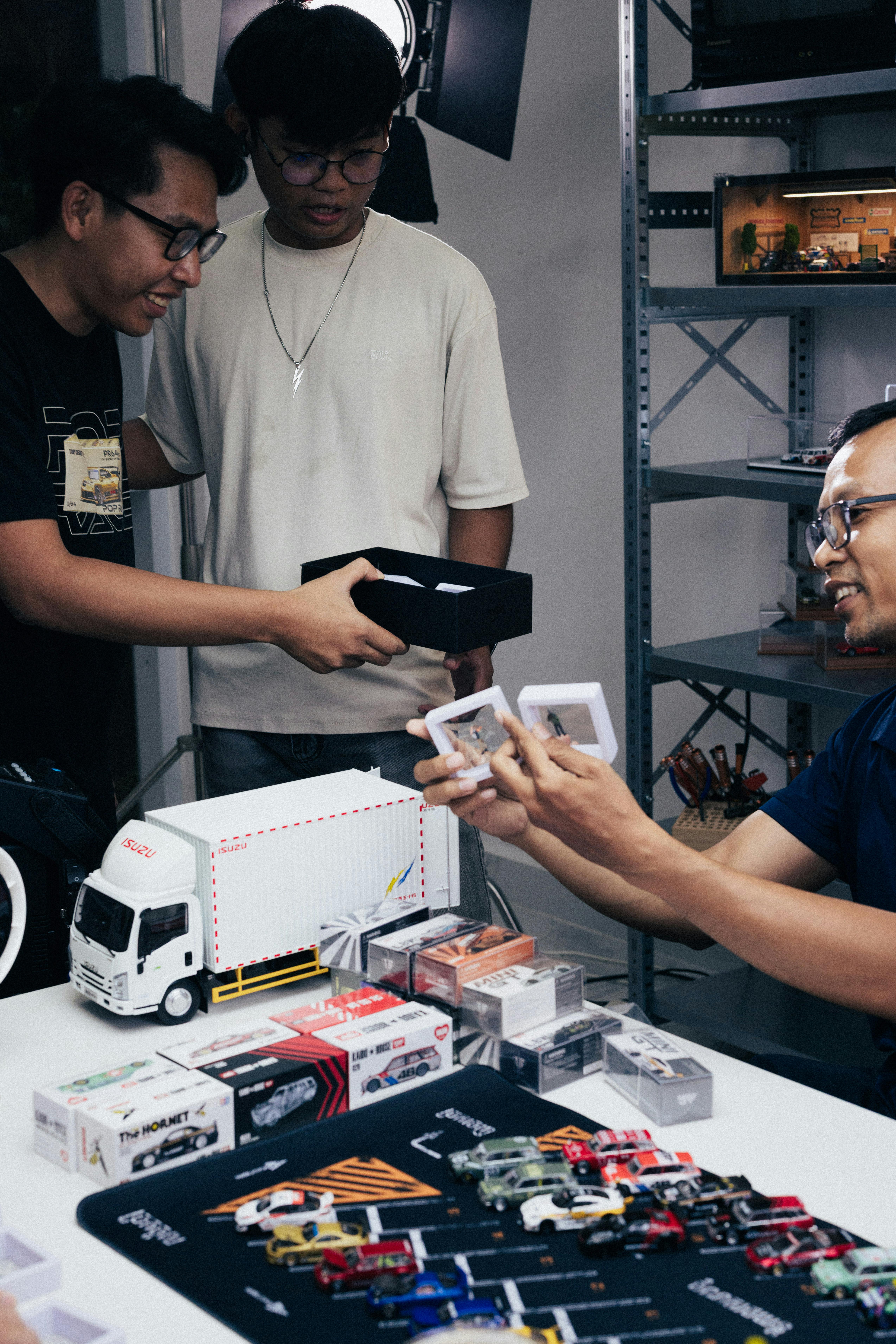 Gratis Sekelompok penggemar mobil mainan sedang memeriksa koleksi diecast terperinci di dalam ruangan di Phnom Penh. Foto Stok