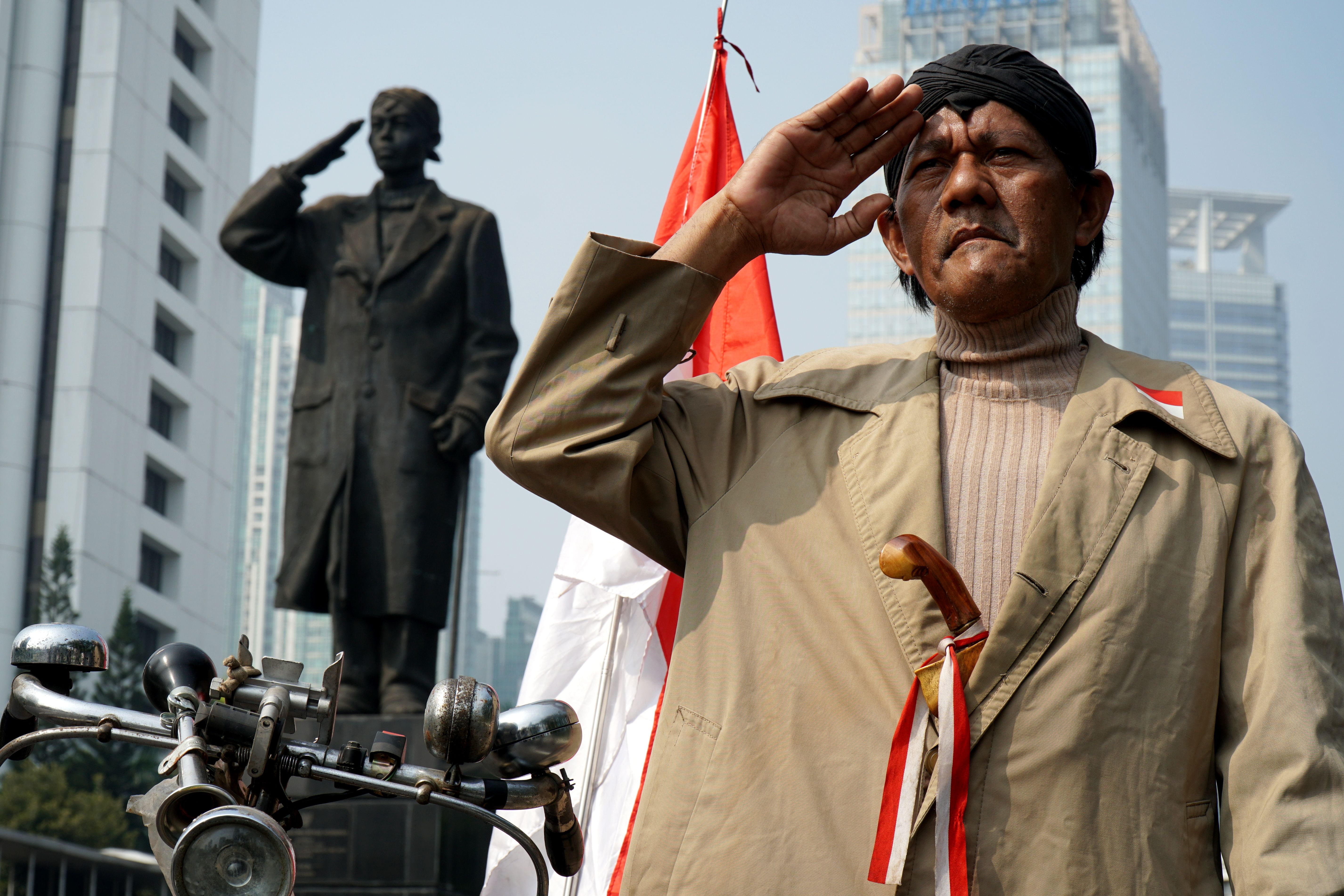 Indonesian man saluting with national flag and monument in Jakarta.