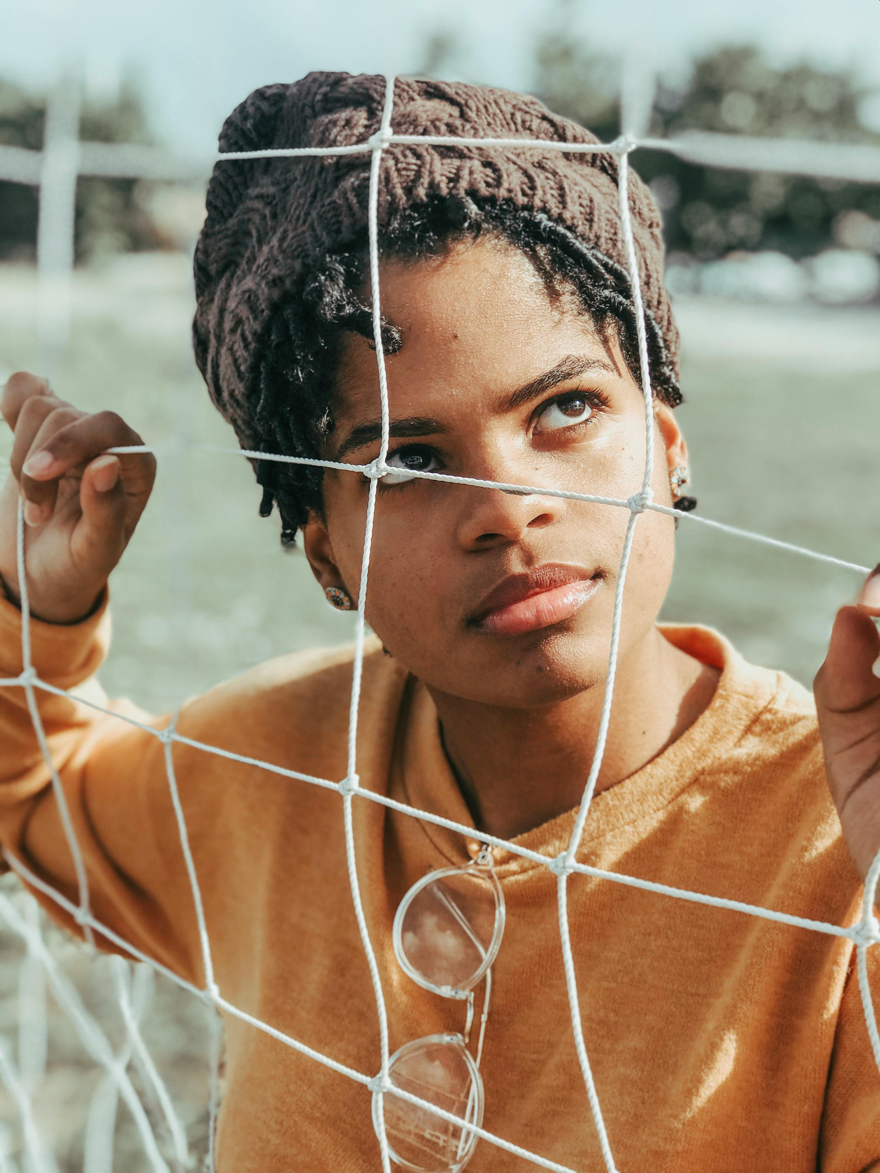 一个戴着针织帽、穿着休闲装的女人在户外透过网子，看起来若有所思