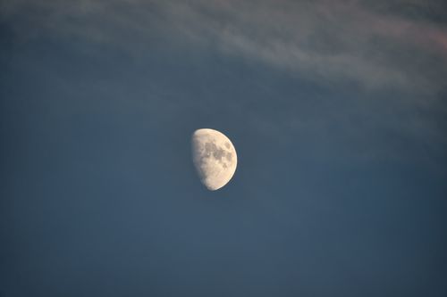 Free A serene half moon set against a partially cloudy night sky, creating a tranquil celestial scene. Stock Photo