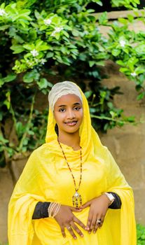 Elegant woman in vibrant yellow traditional attire posing outdoors in nature.