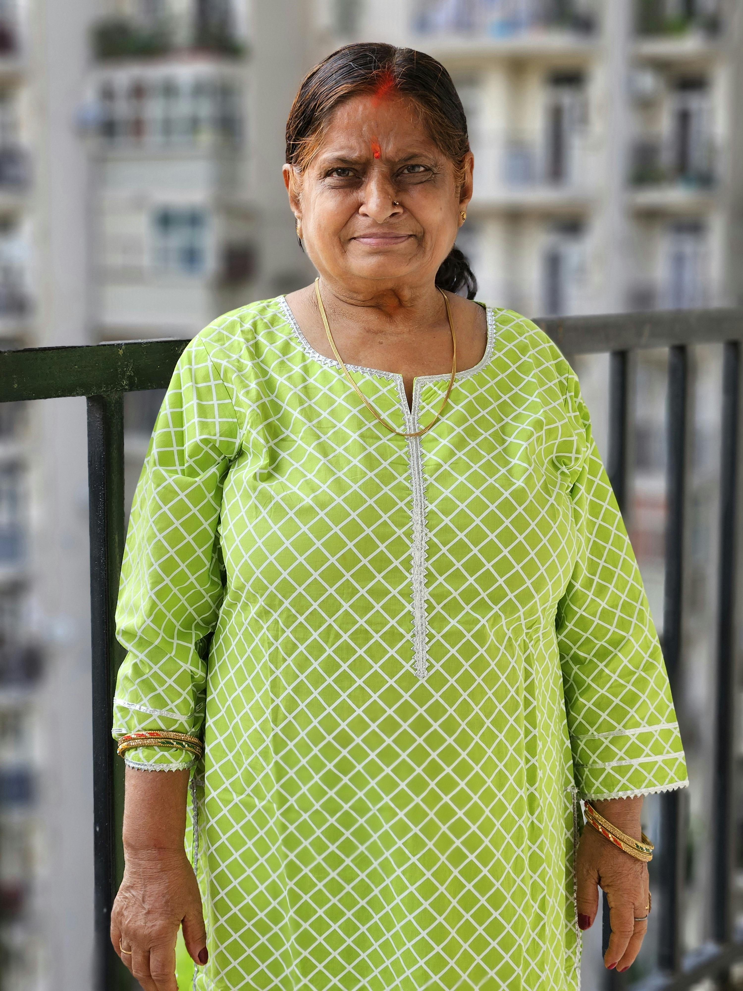 Elderly woman in vibrant green dress smiling outdoors on a balcony.