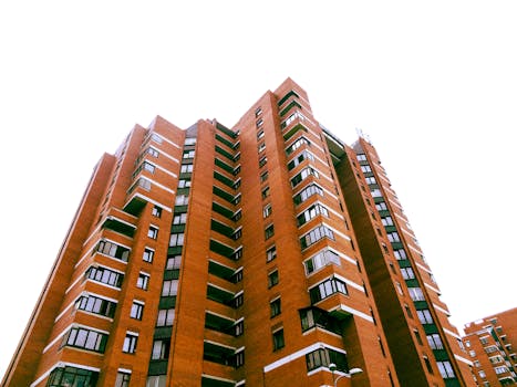 A tall red-brick residential apartment with modern architecture against a clear sky.